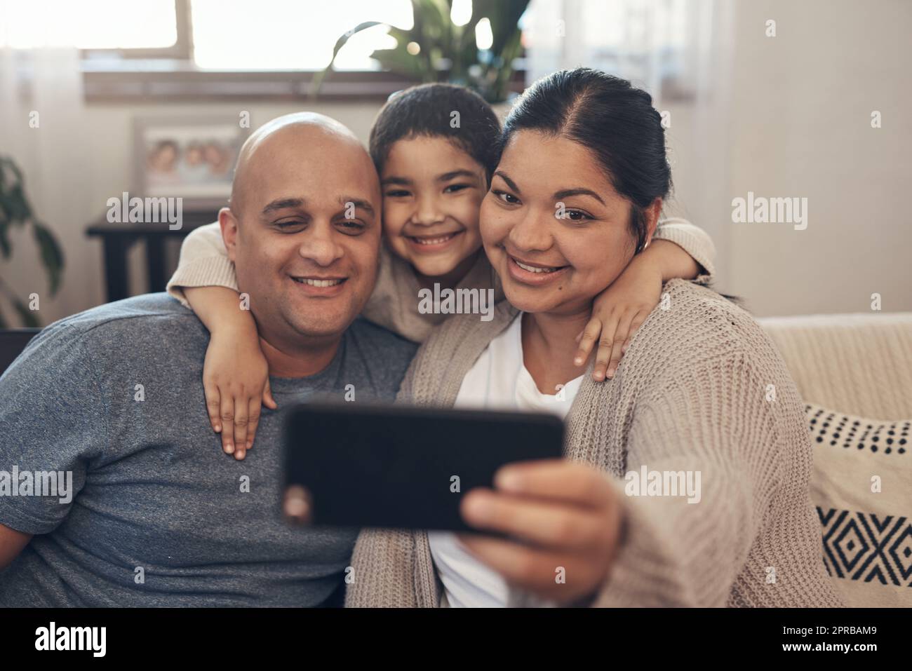 Sorprende la tua famiglia e le ama per sempre. Una giovane famiglia felice che prende selfie con uno smartphone sul divano di casa. Foto Stock