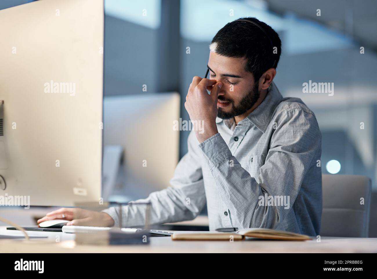 I dipendenti bruciati sono pessimi per il lavoro: Un giovane si sente stressato mentre utilizza un auricolare e un computer a tarda notte in un ufficio moderno. Foto Stock