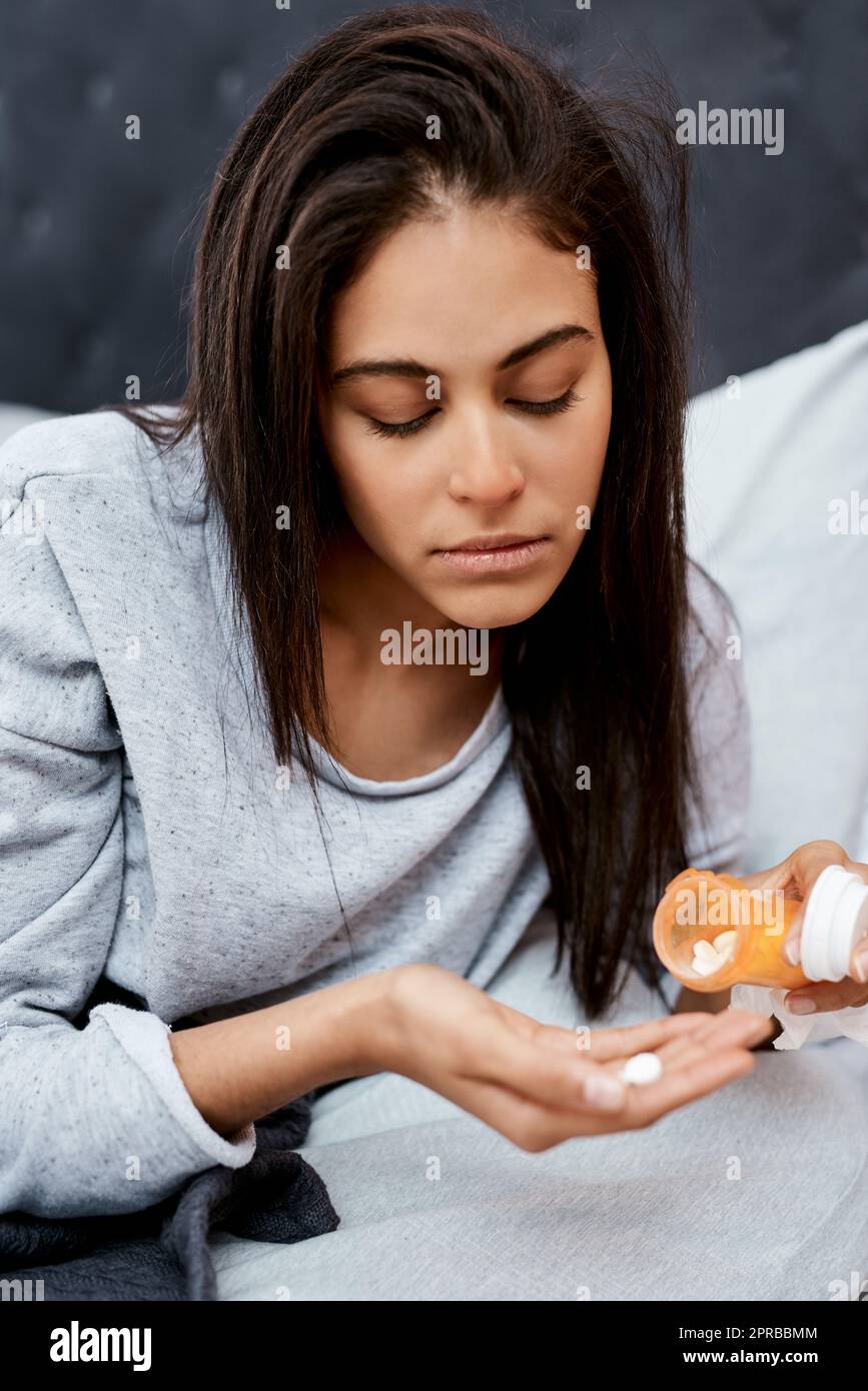 Fate attenzione, la stagione influenzale è qui. Una giovane donna che prende farmaci mentre si recupera da una malattia a letto a casa. Foto Stock
