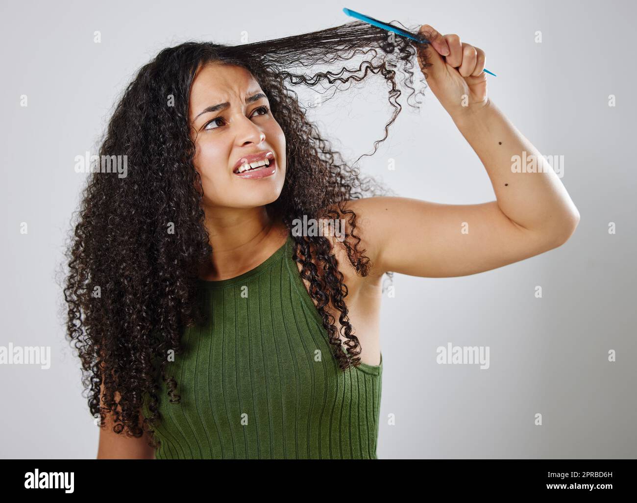 Pettinare i capelli non è mai un compito facile. Una donna accigliata mentre pettina i capelli su uno sfondo grigio. Foto Stock