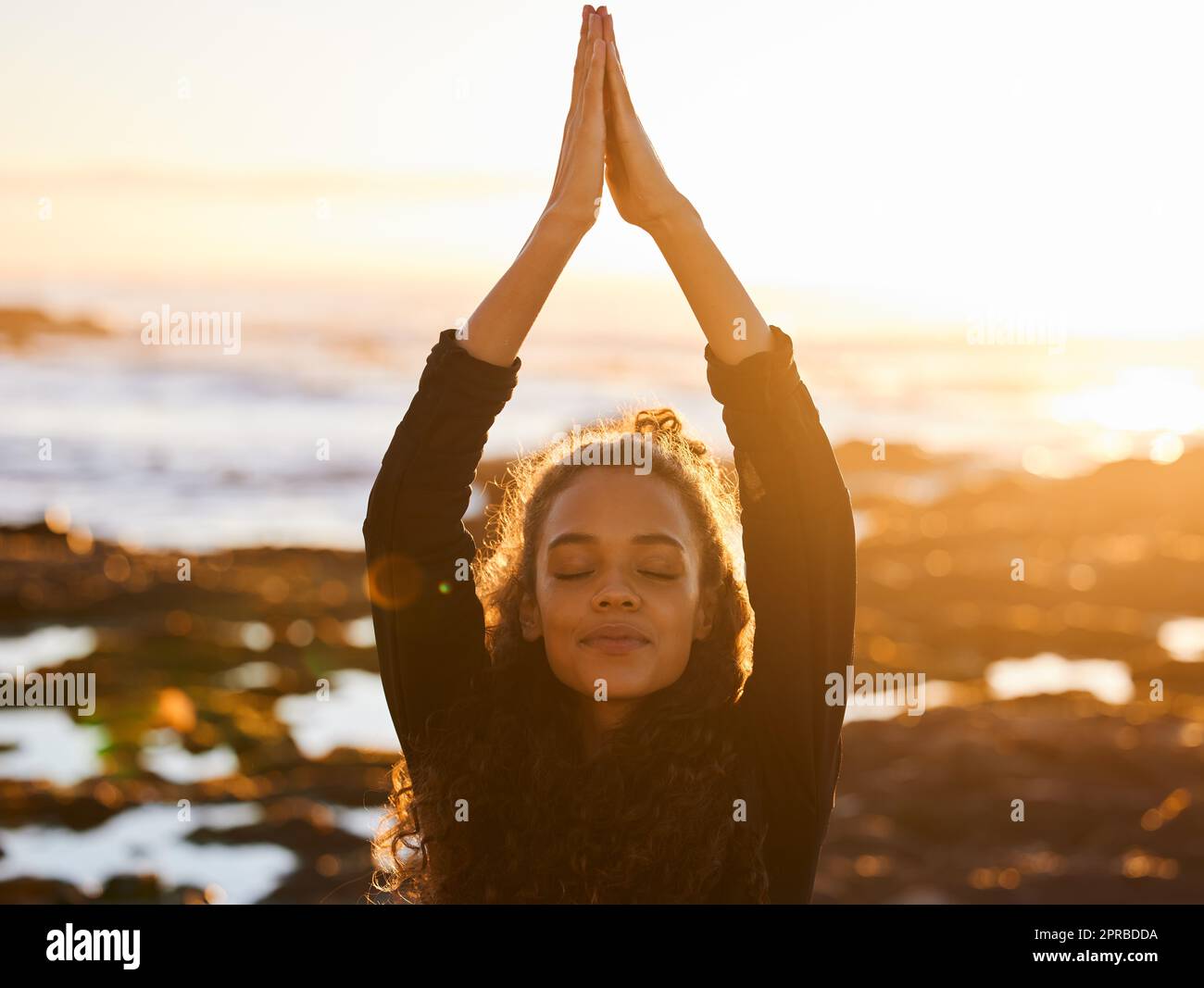 Raccogliere buona energia dall'universo. Una giovane donna attraente che fa yoga da sola sulla spiaggia al tramonto. Foto Stock