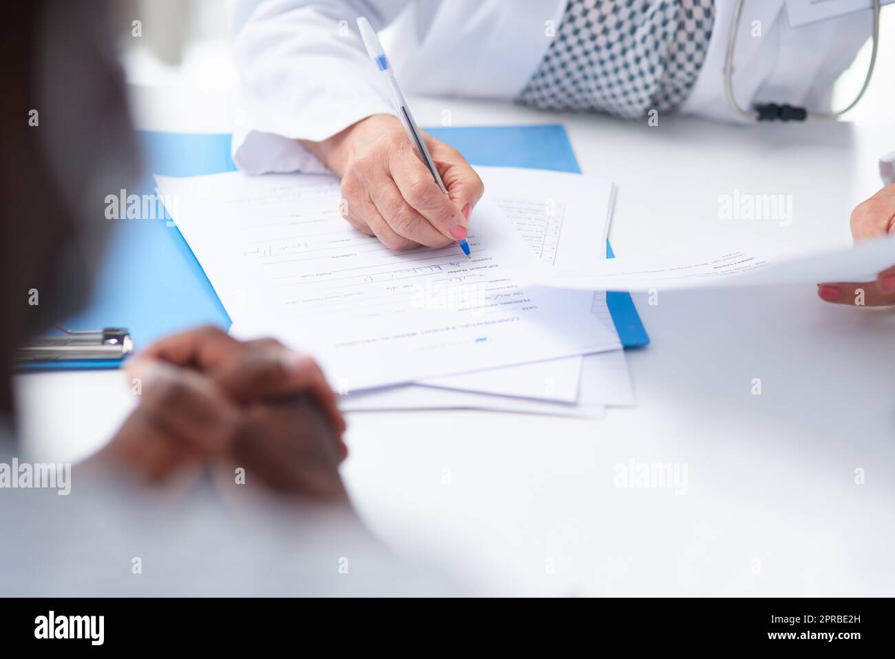 Questa paziente ha una grande assicurazione medica. Una dottore femminile che riempie i documenti del paziente alla sua scrivania. Foto Stock