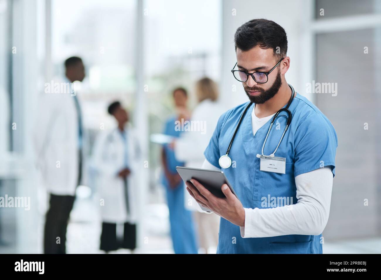 Tuffarsi in alcune ricerche cliniche. Un giovane medico che usa un tablet digitale in un ospedale. Foto Stock