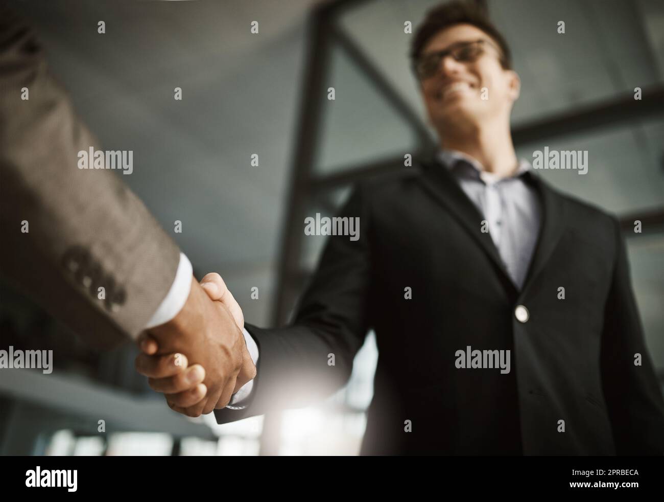 Al di sotto di due uomini d'affari si stringono la mano durante una riunione in un ufficio. I colleghi finalizzano una promozione, un accordo e una fusione di successo. I colleghi salutano mentre collaborano e negoziano durante il colloquio Foto Stock