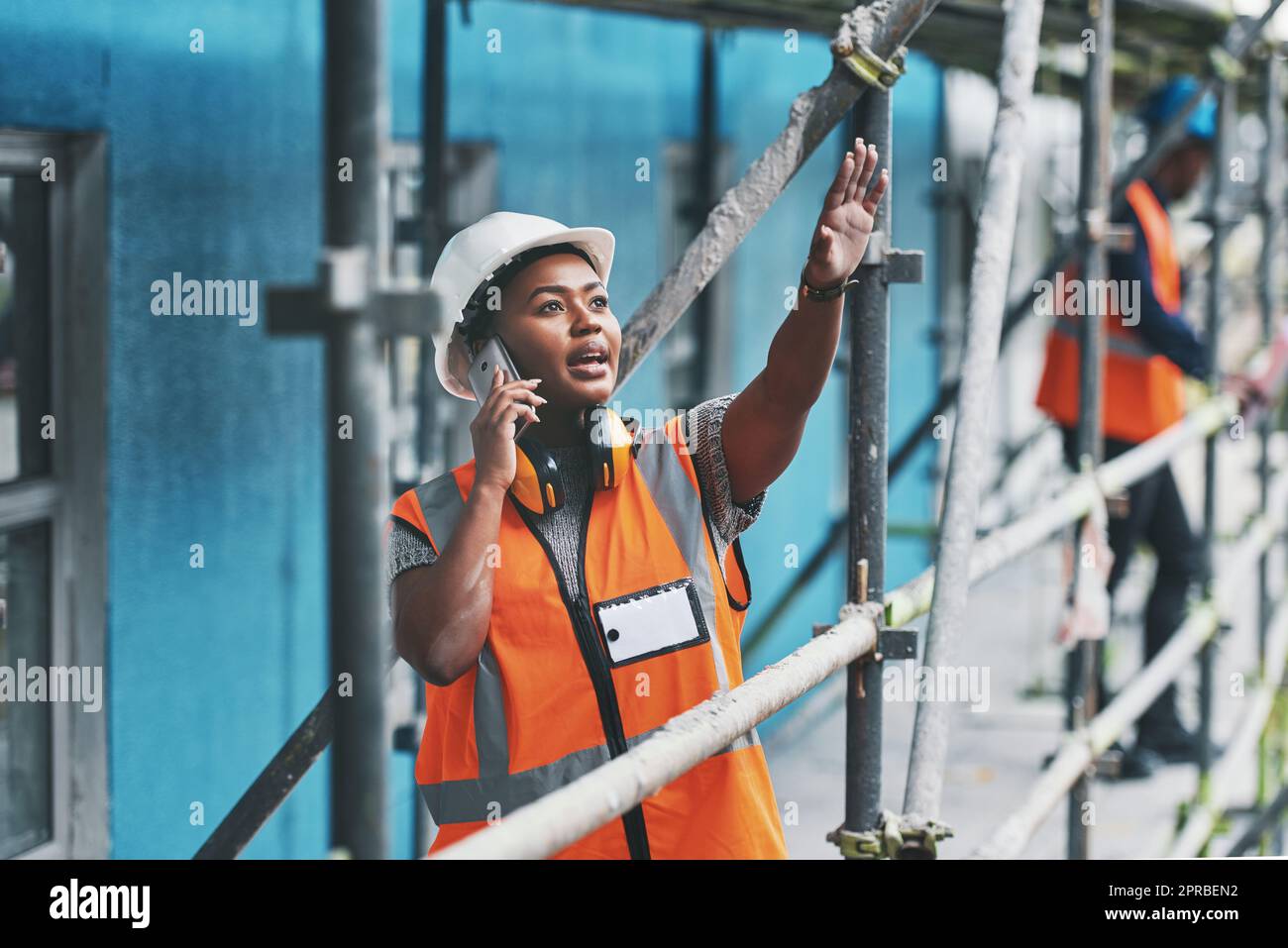 Una giovane donna che parla su un cellulare mentre lavora in cantiere. Foto Stock