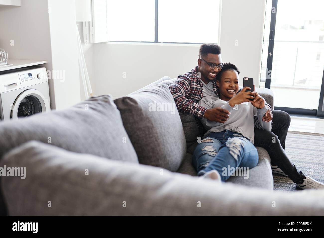 Scorrendo attraverso tutti i memi divertenti. Una giovane coppia che usa un cellulare mentre si rilassa su un divano a casa. Foto Stock