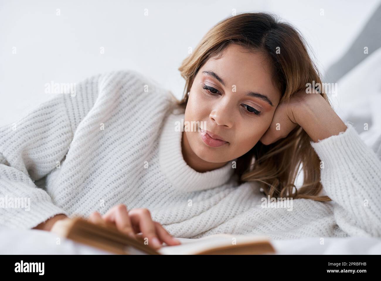Quando avete un po' di tempo libero, leggete: Una giovane donna che legge un libro mentre si trova sul suo letto. Foto Stock