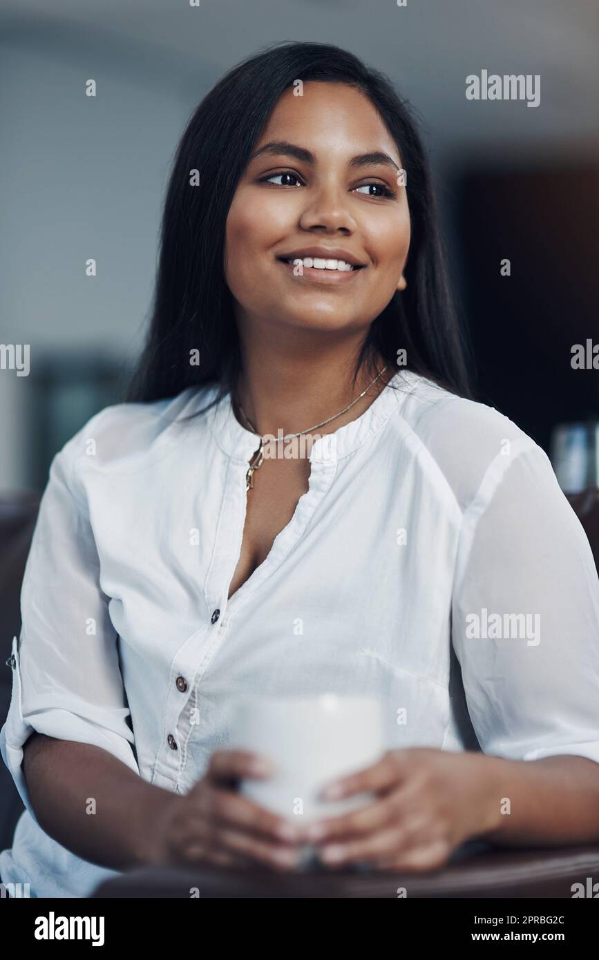 Una giovane donna d'affari che beve caffè mentre si fa una pausa in ufficio, si respira prima di tornare ai suoi piani di successo. Foto Stock