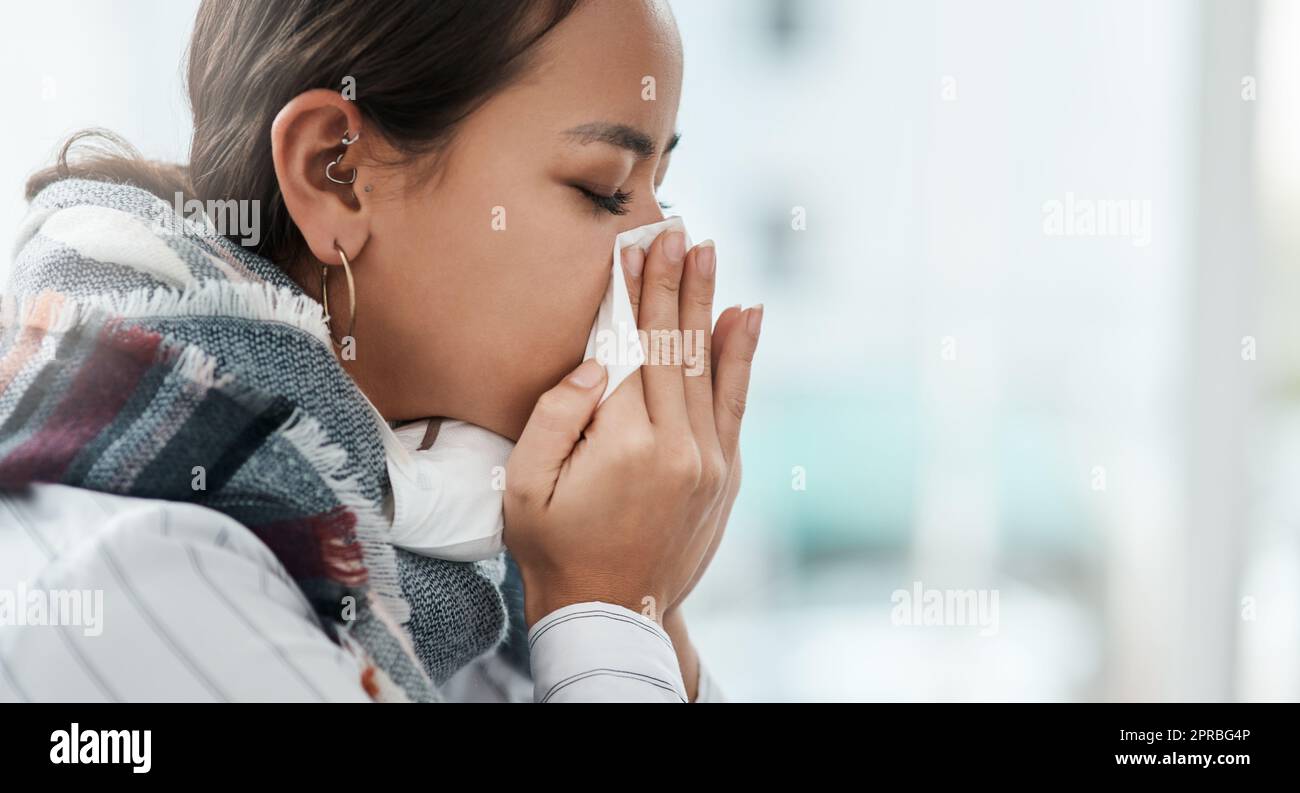 Ricordate quando era solo l'influenza. Una giovane donna d'affari che soffia il naso in un ufficio moderno. Foto Stock
