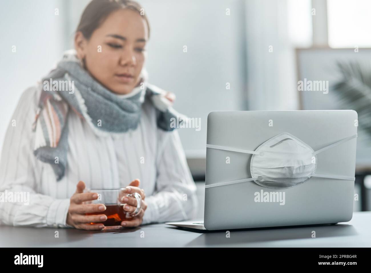 Un po' di malattia non fa deragliare il suo viaggio verso il successo. Una giovane donna d'affari che ha un bicchiere di tè alle erbe alla sua scrivania in un ufficio moderno. Foto Stock