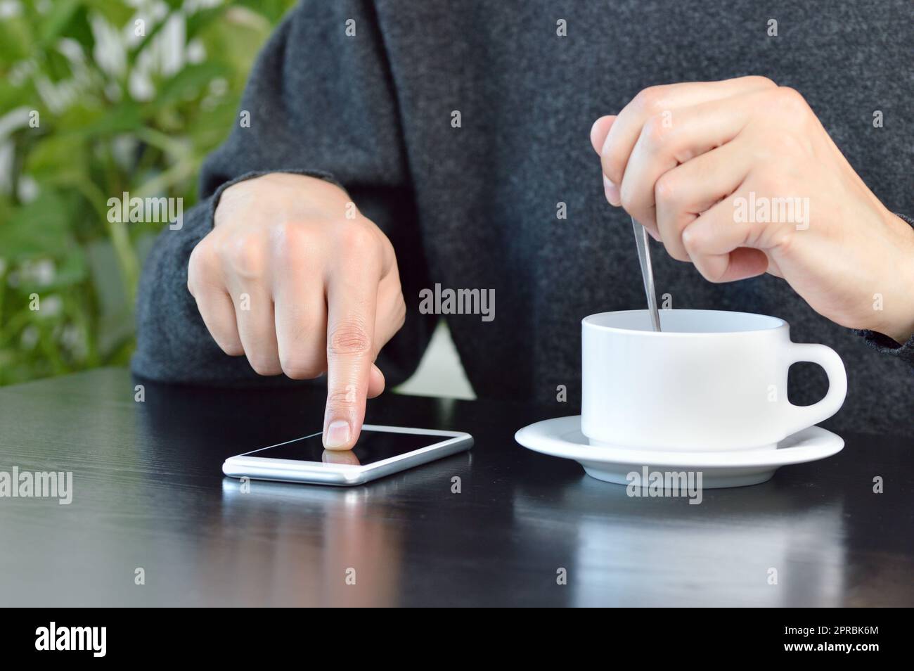 Primo piano di un giovane utilizzando un cellulare e bevendo un caffè mentre si siede in un bar Foto Stock