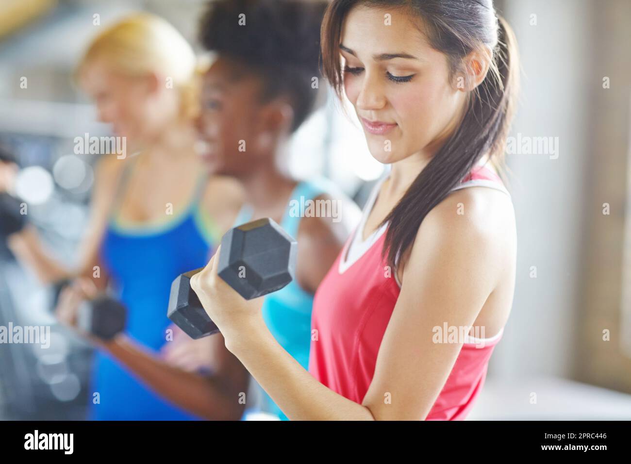 Mi chiedo se il formatore sa quanto sia leggero. Un colpo una donna attraente che guarda giù mentre si lavora con due donne nel backgroung. Foto Stock Mi chiedo se il formatore sa quanto sia leggero. Un colpo una donna attraente che guarda giù mentre si lavora con due donne nel backgroung. Foto Stock