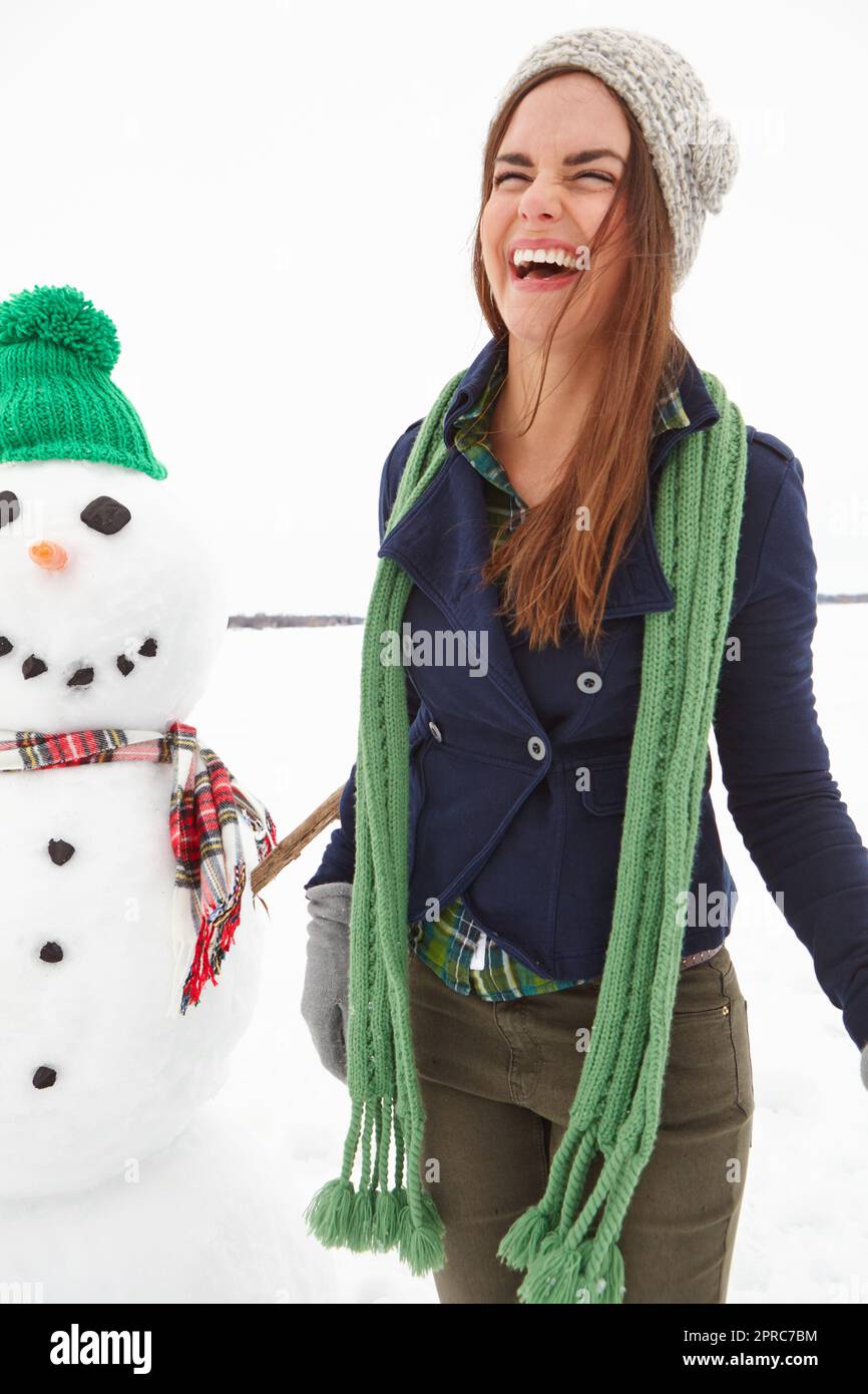 A shes piace stare fuori sulla neve. Un colpo di tre quarti di lunghezza di una giovane donna in piedi davanti a un pupazzo di neve. Foto Stock