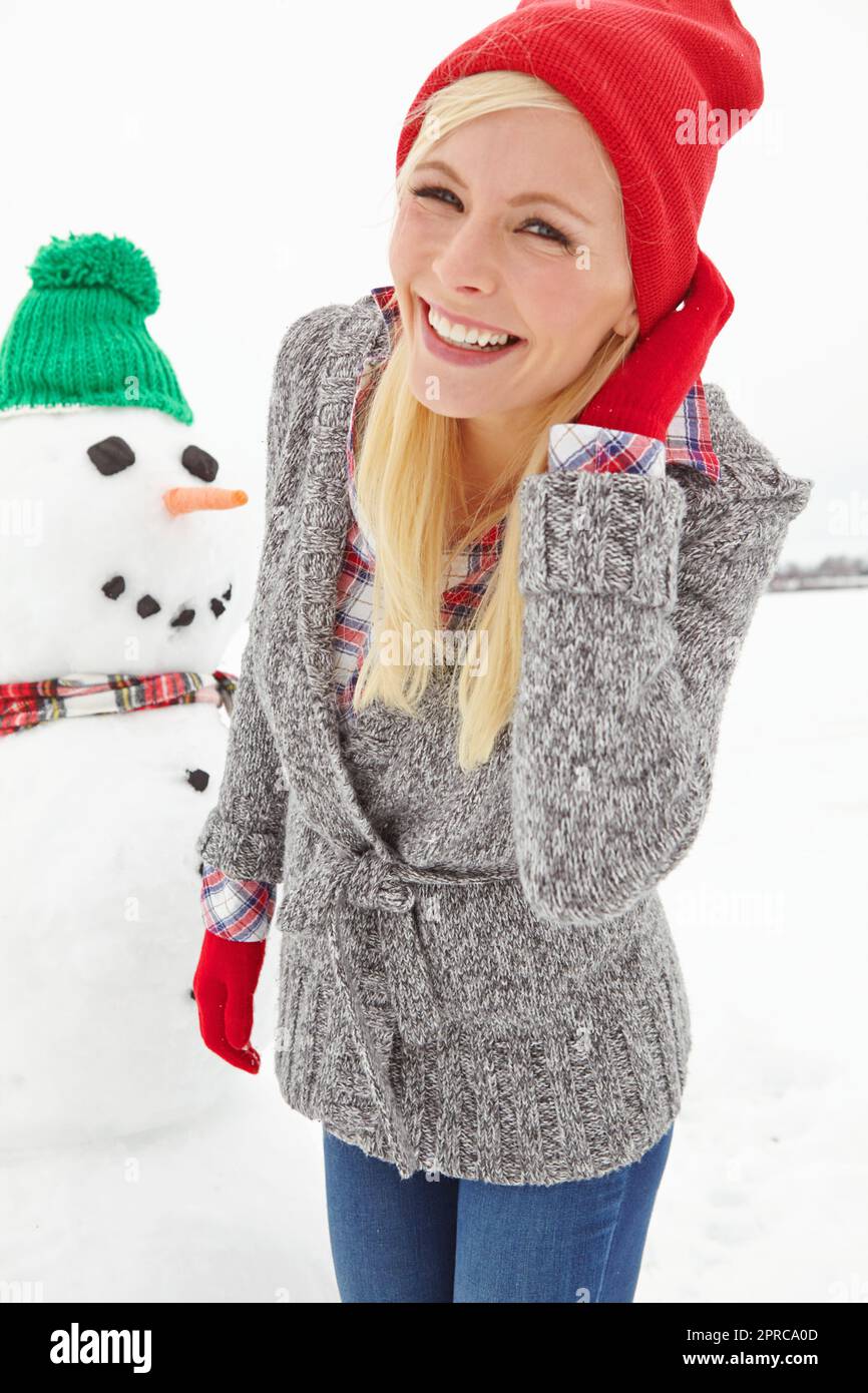 Concedetevi una giornata di divertimento per le feste invernali. Un colpo di tre quarti di lunghezza di una bella giovane donna in piedi davanti ad un pupazzo di neve. Foto Stock