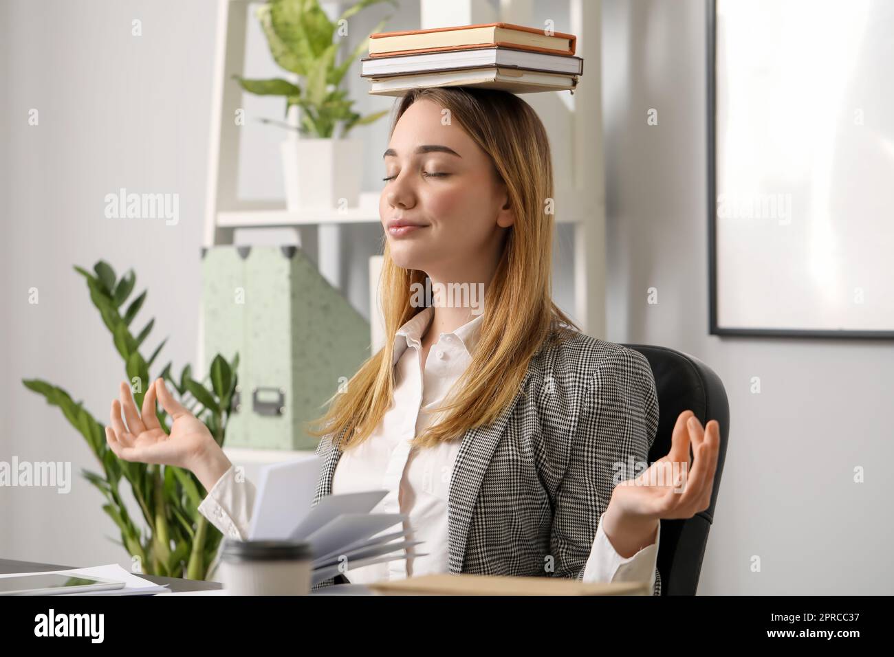 Giovane donna d'affari che medita con i libri in ufficio. Concetto di equilibrio Foto Stock