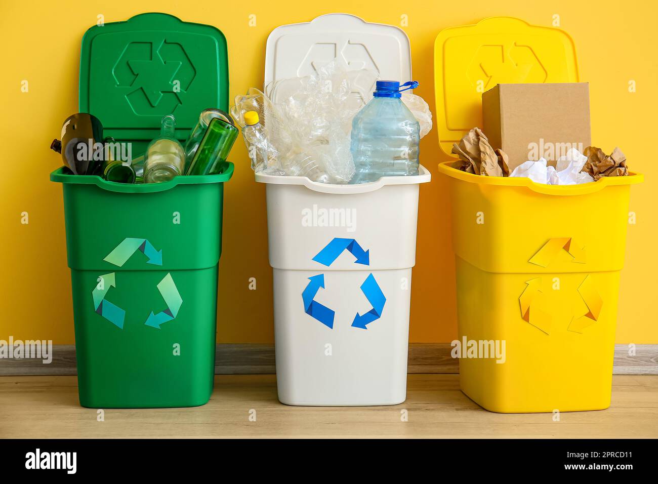 Bidoni dei rifiuti con simbolo di riciclaggio e rifiuti diversi vicino alla parete gialla Foto Stock