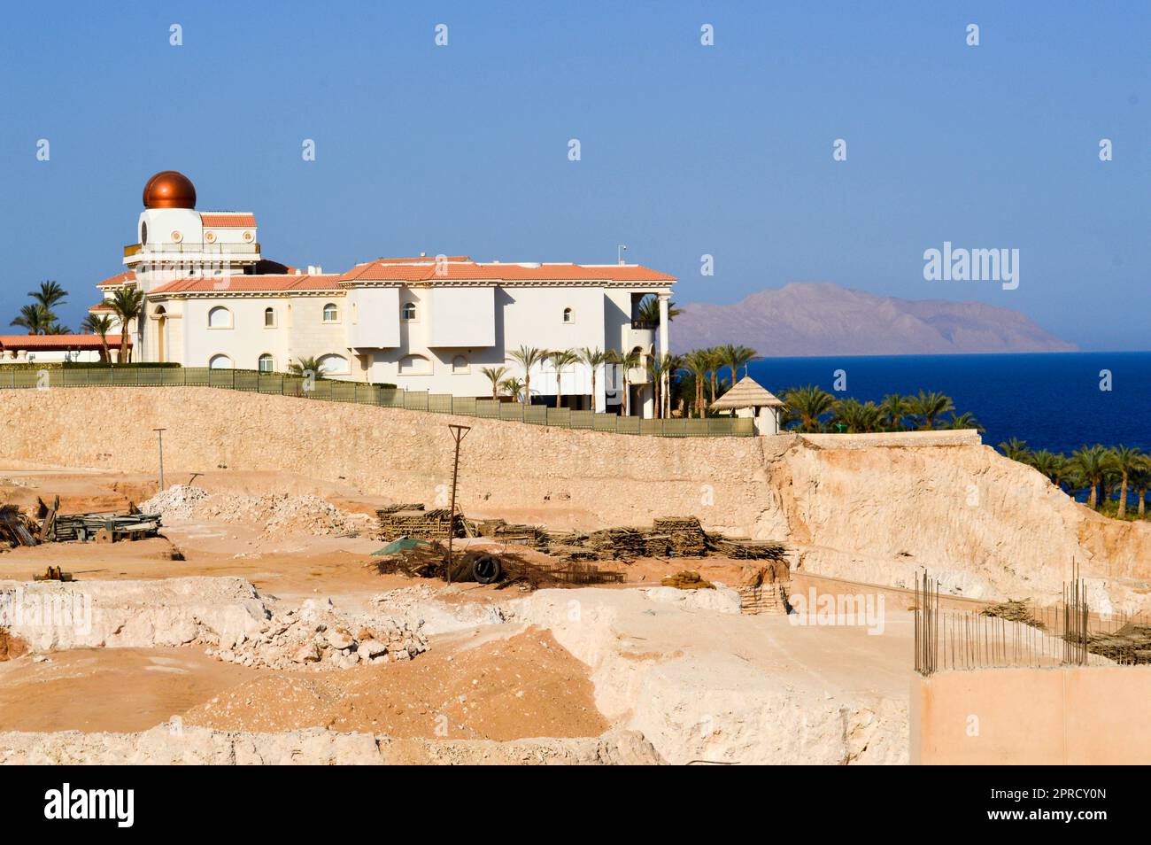 Costruzione dell'hotel sullo sfondo di un planetario con una cupola dorata sulla riva blu del mare sullo sfondo di palme e montoni Foto Stock