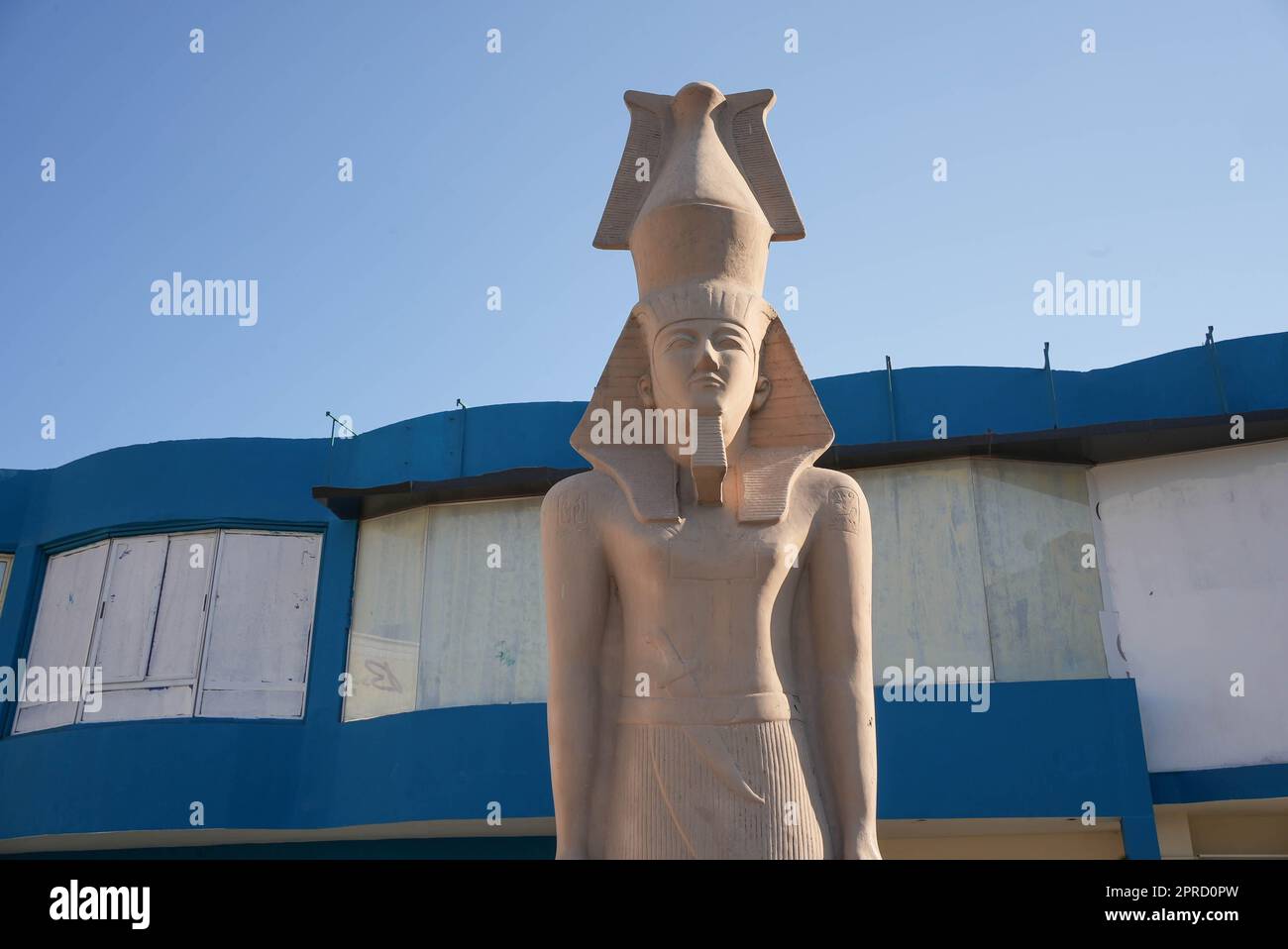 Un'antica statua egiziana di fronte a un edificio blu Foto Stock