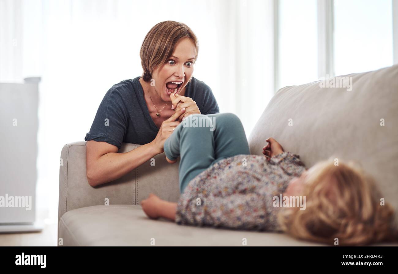Im andare a mangiare le dita dei piedi. Una giovane madre attraente e giocare con sua figlia nel soggiorno di casa. Foto Stock