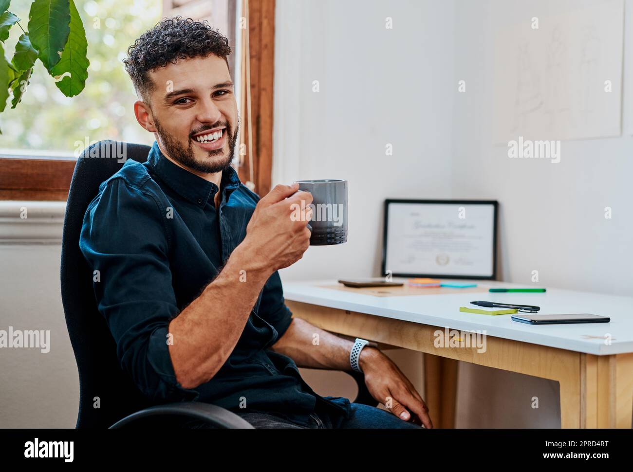 Un lavoro ben fatto merita una buona tazza di caffè. Un giovane uomo d'affari che ha una pausa caffè alla sua scrivania in un ufficio moderno. Foto Stock