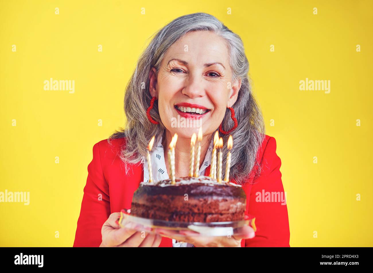 La vita è piena di piccoli momenti dolci. Ritratto di una donna anziana allegra che tiene una torta di compleanno su uno sfondo giallo. Foto Stock
