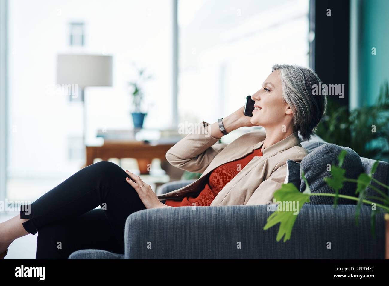 Ascoltare le richieste dei miei clienti. Una donna d'affari matura attraente seduta da sola e che parla sul suo cellulare nel suo ufficio domestico. Foto Stock