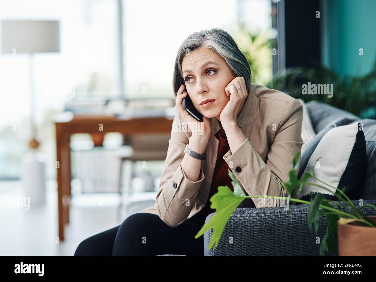 Che cosa sto andando fare. Una donna d'affari matura attraente seduta da sola e che parla sul suo cellulare nel suo ufficio domestico. Foto Stock