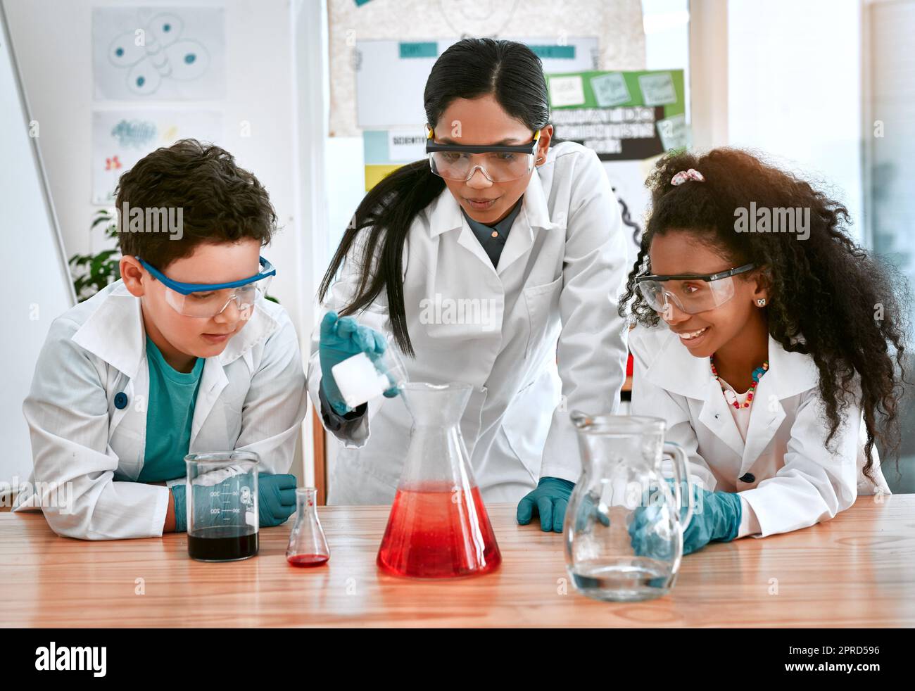 Scoprire le meraviglie del mondo con la scienza. Un adorabile ragazzino e ragazza che conduce un esperimento scientifico con il loro insegnante a scuola. Foto Stock