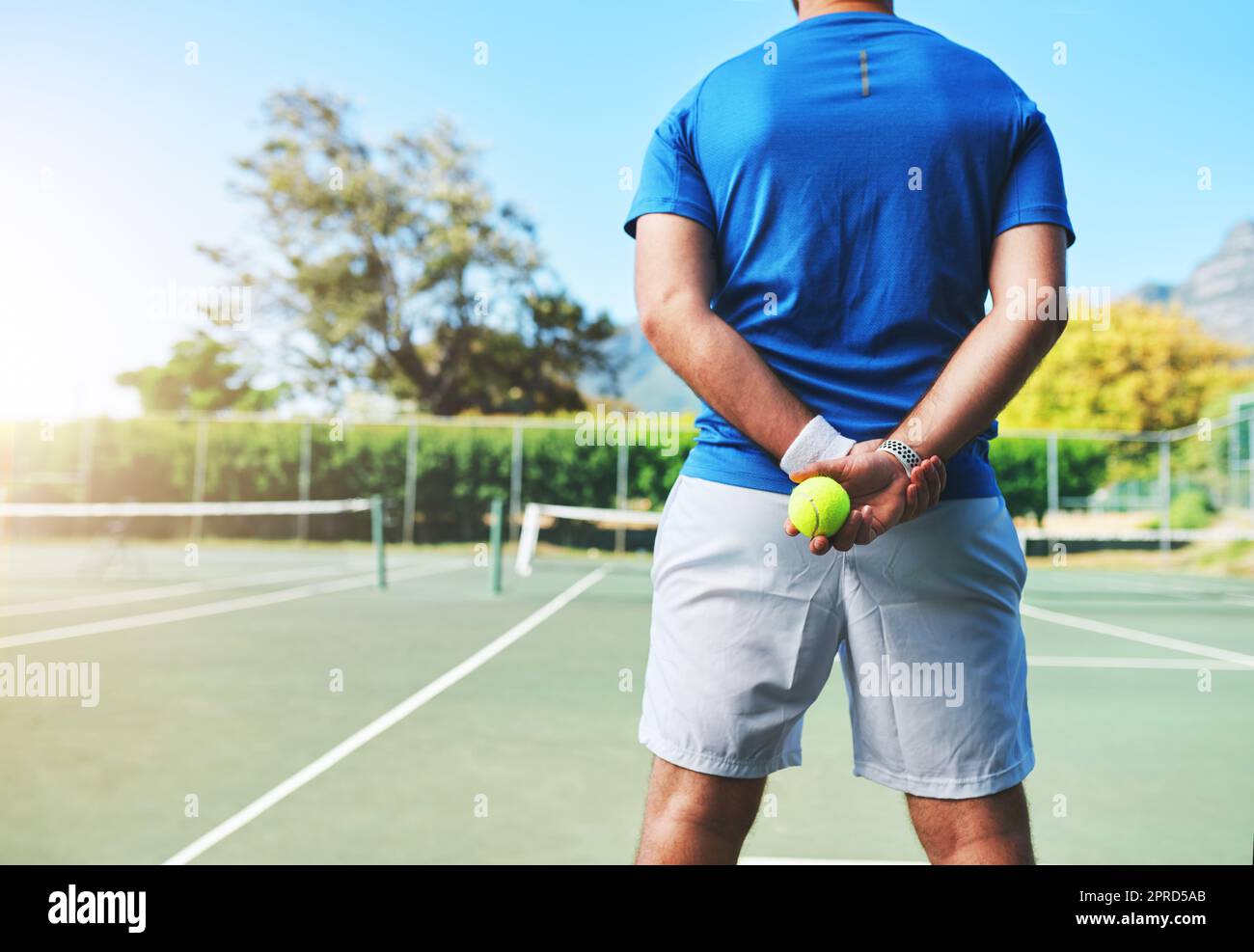 Il gioco ottenuto permette di giocare. Tiro da dietro di un giocatore di tennis maschile irriconoscibile che tiene una palla da tennis su un campo all'aperto. Foto Stock