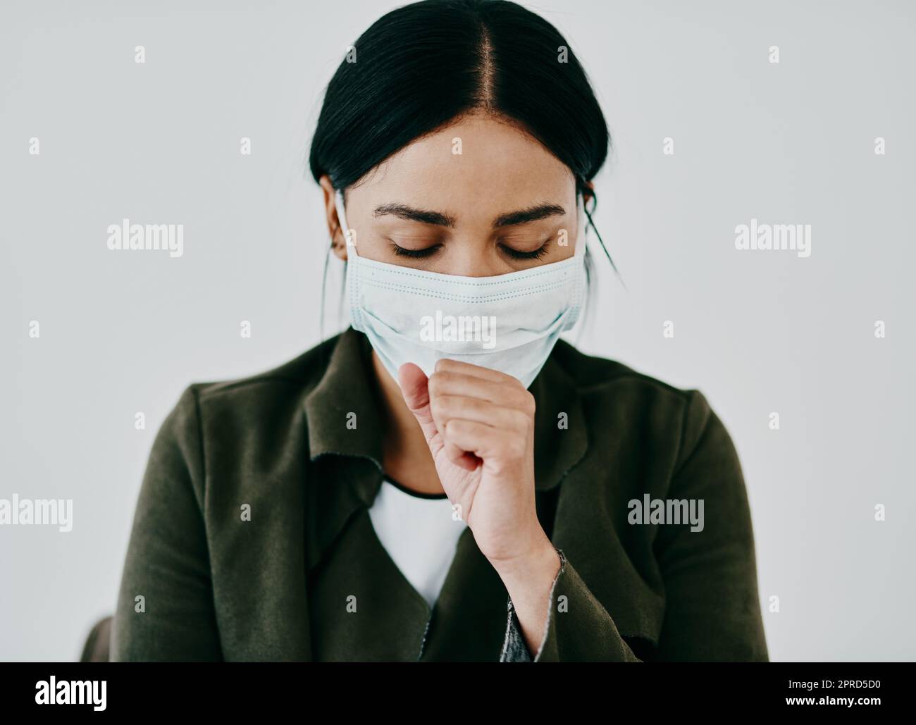 È una tosse o qualcosa di più grave, una giovane donna che tosse e indossa una maschera contro uno sfondo studio. Foto Stock