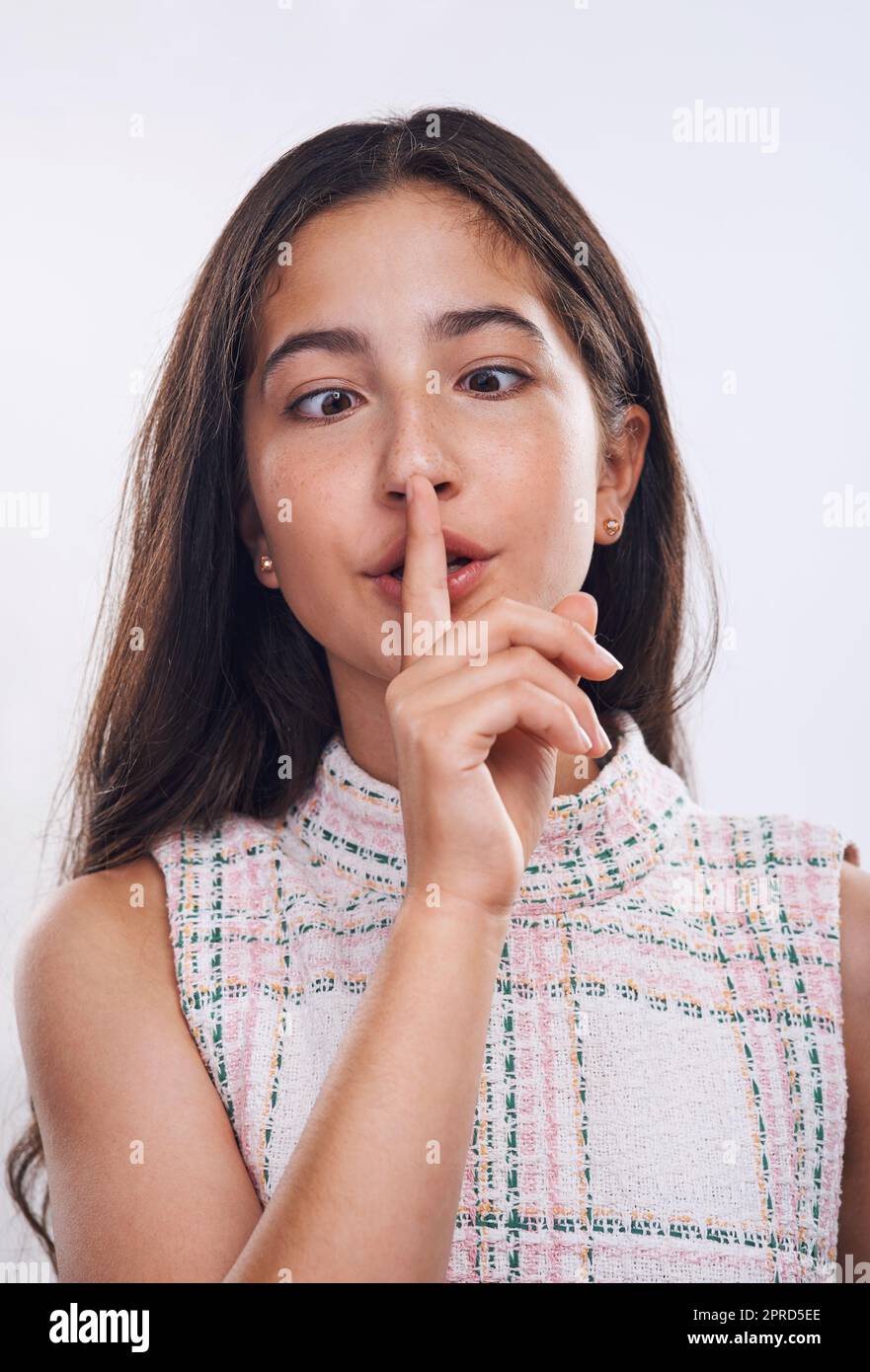 Siate voi stessi. Una ragazza adolescente attraente in piedi con il dito sulle labbra contro uno sfondo bianco studio. Foto Stock