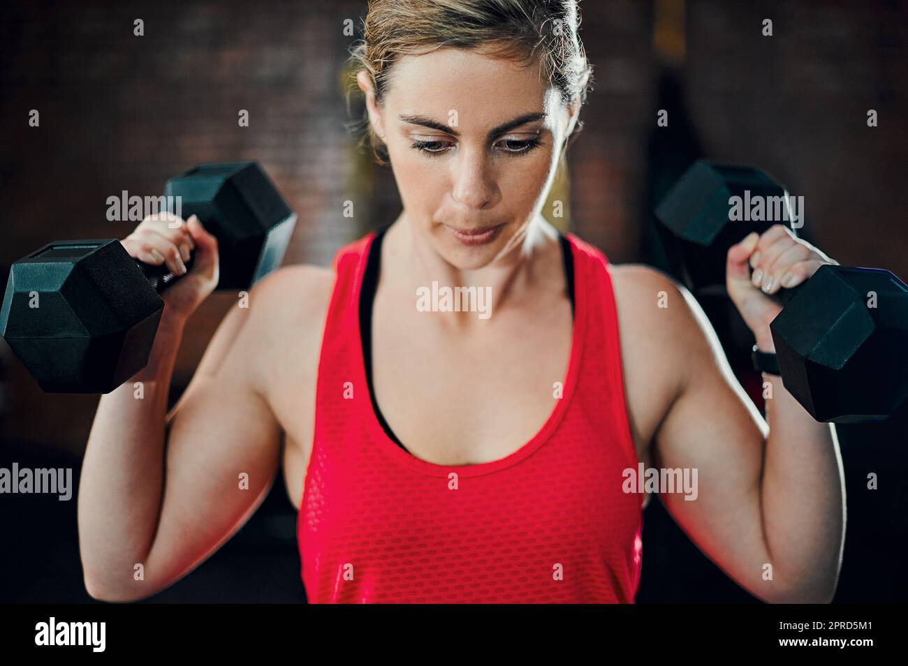 Il suo tempo per far funzionare quei muscoli. Una giovane atleta attraente che si allena con i manubri in palestra. Foto Stock