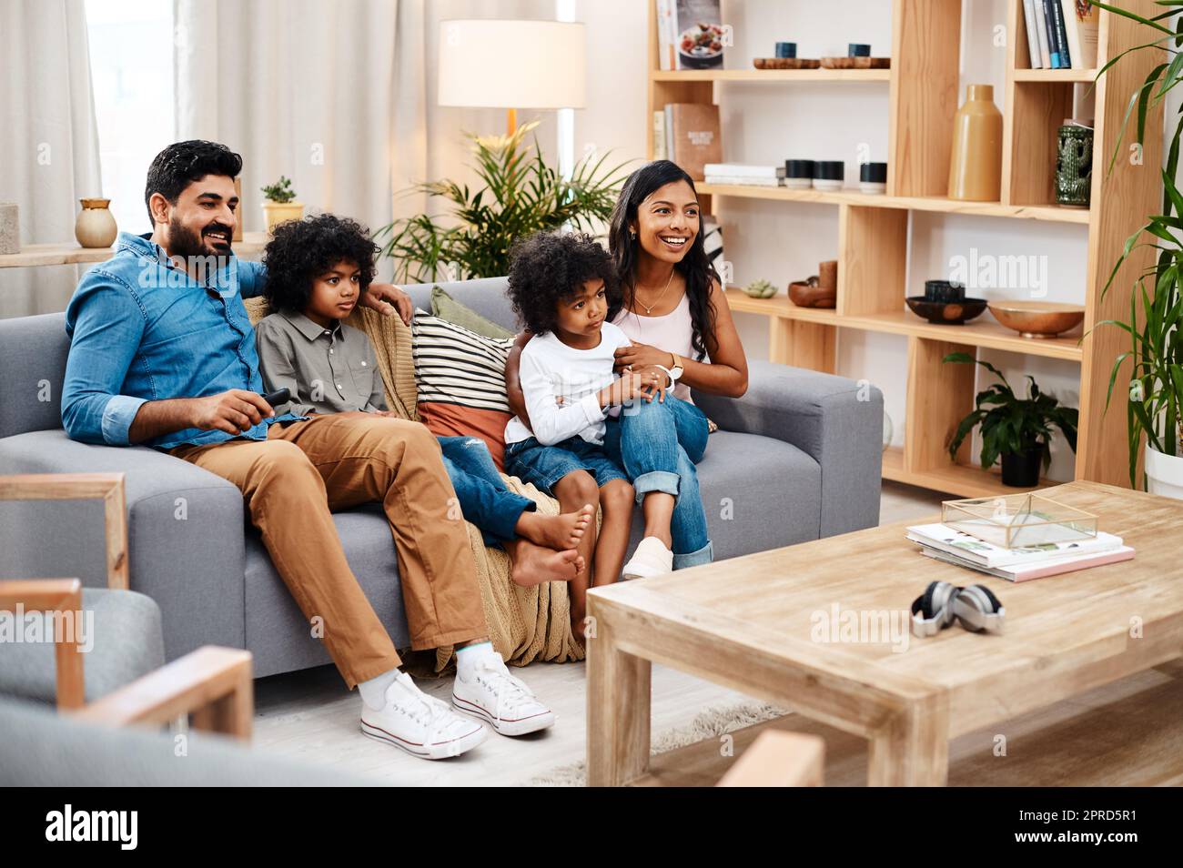 Guardare film è un'attività familiare. Scatto a tutta lunghezza di una bella giovane famiglia seduta sul divano e guardando la tv insieme a casa. Foto Stock