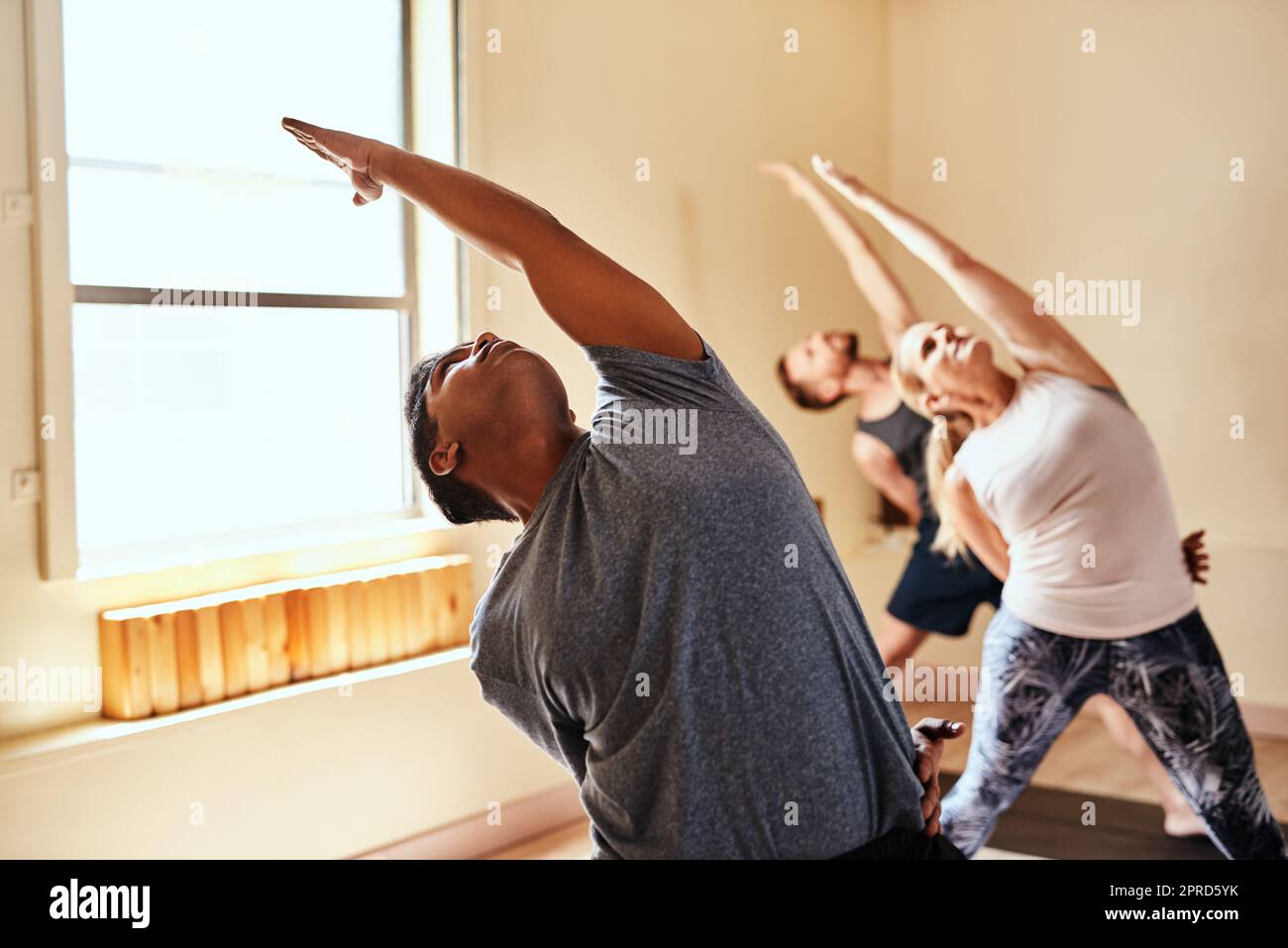 Sciogliere il corpo, allentare la mente. Un gruppo di giovani uomini e donne che praticano lo yoga in una lezione di fitness. Foto Stock