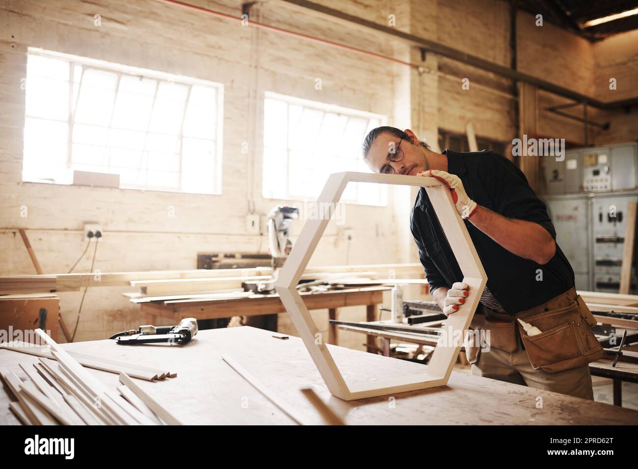 L'attenzione al dettaglio è fondamentale in questo settore. Un carpentiere giovane bello che lavora su una cornice di legno all'interno di un'officina. Foto Stock