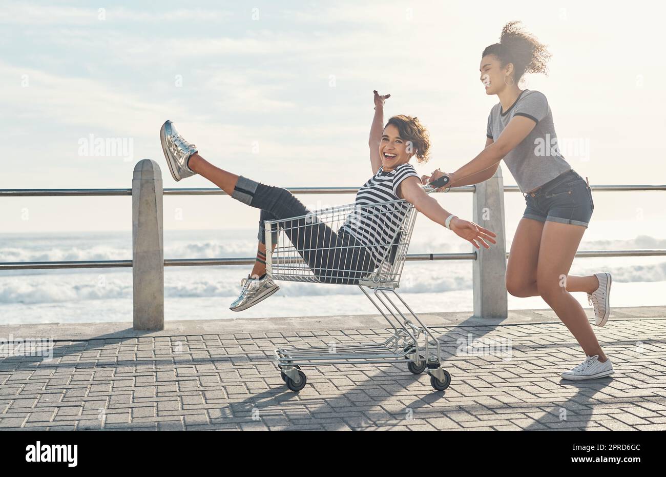 La vita sarebbe così noiosa senza amici: Una giovane donna che spinge la sua amica sul lungomare in una carta dello shopping. Foto Stock