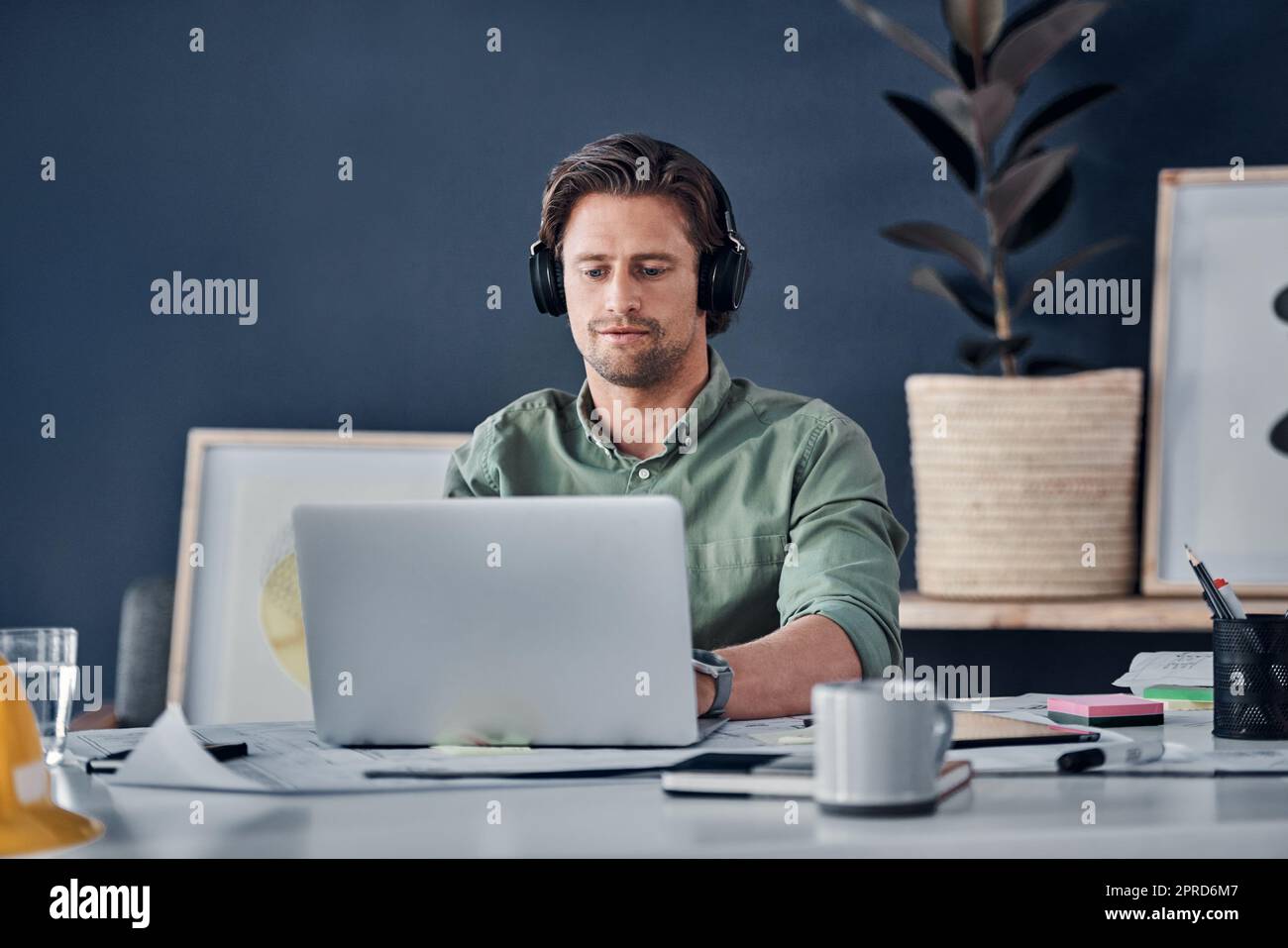 Blocca tutte le distrazioni e concentrati sul successo. Ritratto di un bel giovane uomo d'affari che indossa cuffie mentre lavora su un notebook nel suo ufficio. Foto Stock