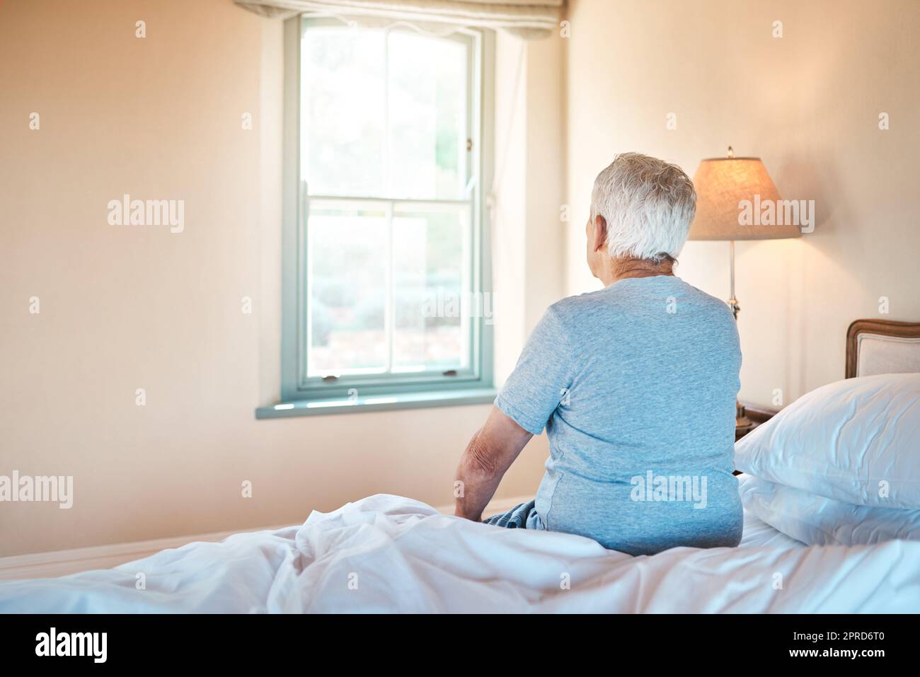 Vita in una casa di riposo. Un anziano irriconoscibile seduto da solo sul bordo del suo letto in una casa di cura. Foto Stock