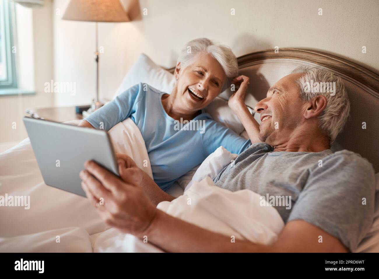 Mi ricordo di questo giorno come se fosse ieri. Una coppia anziana felice seduta insieme a letto e utilizzando un tablet in una casa di cura. Foto Stock