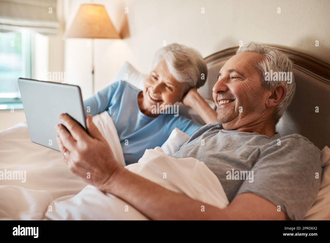 Sembra un buon film da guardare. Una coppia anziana felice seduta insieme a letto e utilizzando un tablet in una casa di cura. Foto Stock