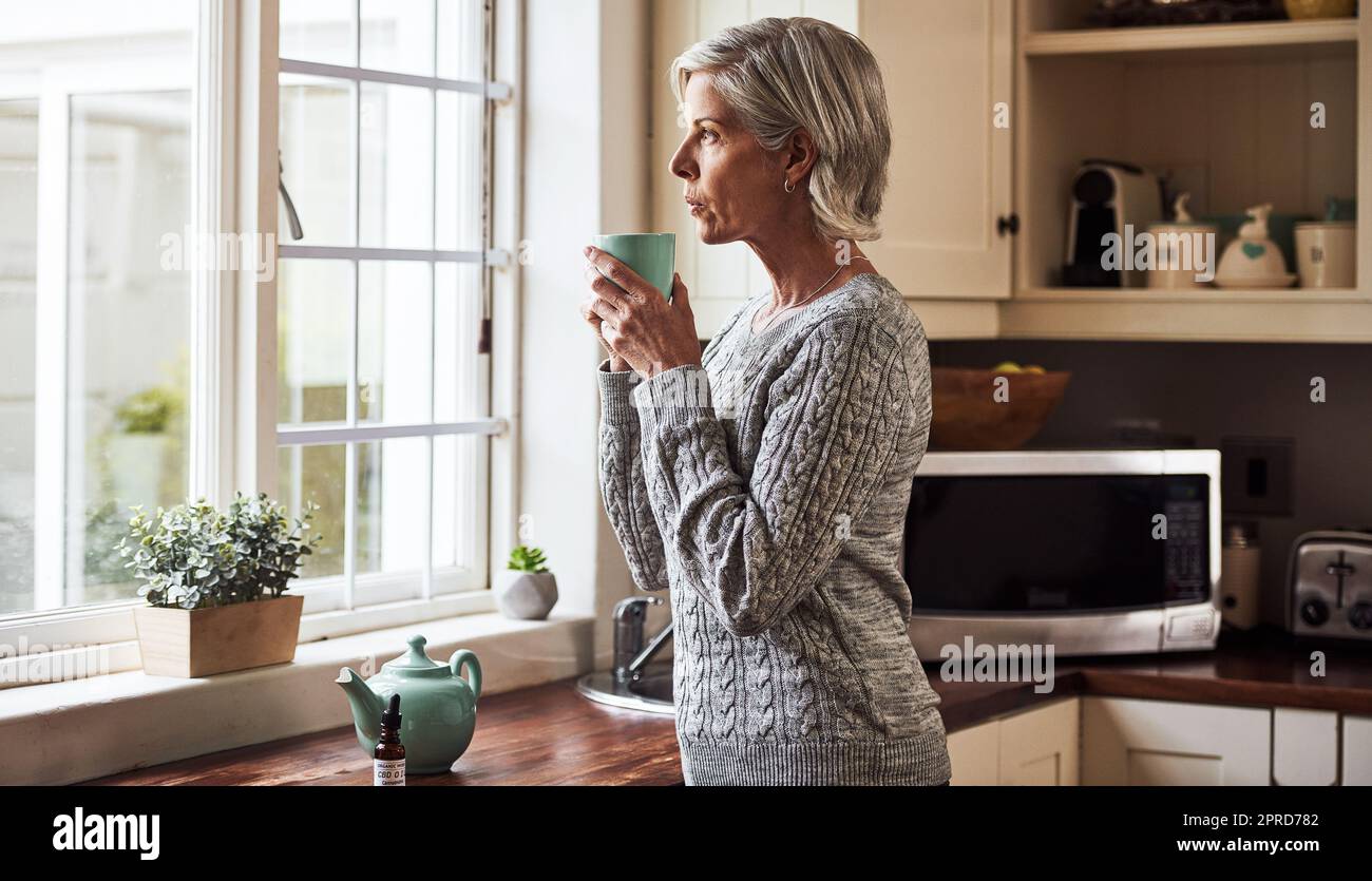 Avevo bisogno di questa tazza. Una donna anziana rilassata che preparava una tazza di tè con olio CBD all'interno di essa a casa durante il giorno. Foto Stock