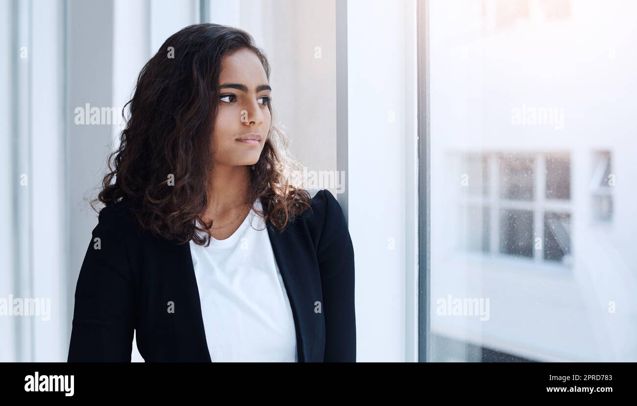 Ponderando sulla sua prossima mossa di affari. Una giovane donna d'affari che guarda fuori la finestra in un ufficio. Foto Stock