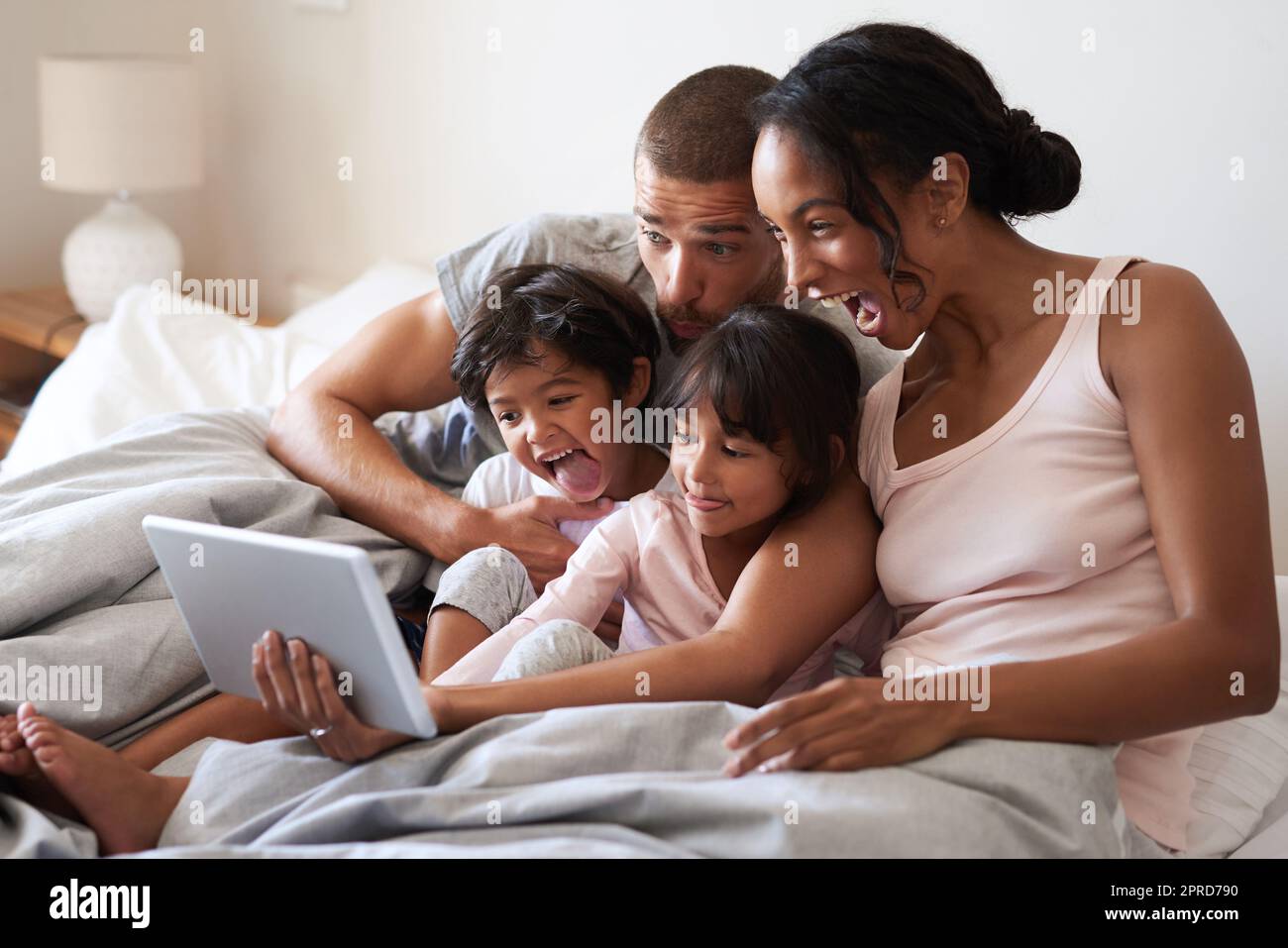Cattura ogni momento meraviglioso con loro. Una famiglia giovane di quattro persone che prende selfie con un tablet digitale in camera da letto. Foto Stock