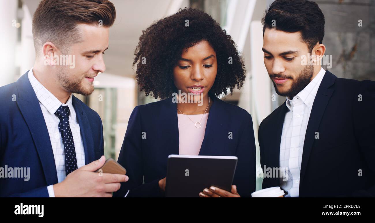Un'ultima volta, tre uomini d'affari in piedi e che lavorano su un tablet mentre sono in ufficio durante il giorno. Foto Stock