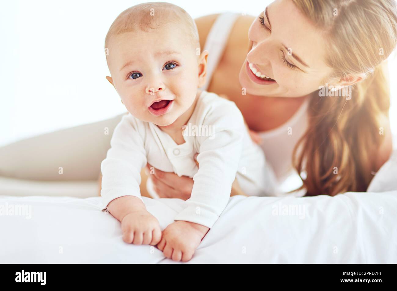 Madre e bambino carino e neonato che si uniscono come una famiglia in camera da letto a casa. Mamma e figlio felici, sorridenti e spensierati che mostrano amore e affetto mentre si rilassano su un letto la mattina Foto Stock