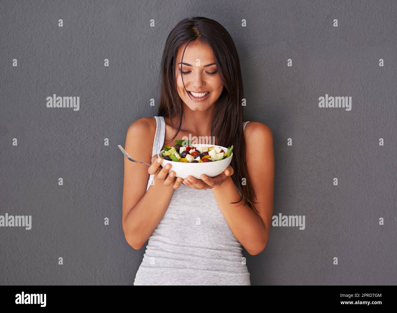 Giovane donna sana che mangia il suo piatto di insalata di cibo fresco. Bella donna sorridente che tiene in mano e si diverte a mangiare il suo piatto verde pulito di verdure come parte del suo stile di vita vegano Foto Stock