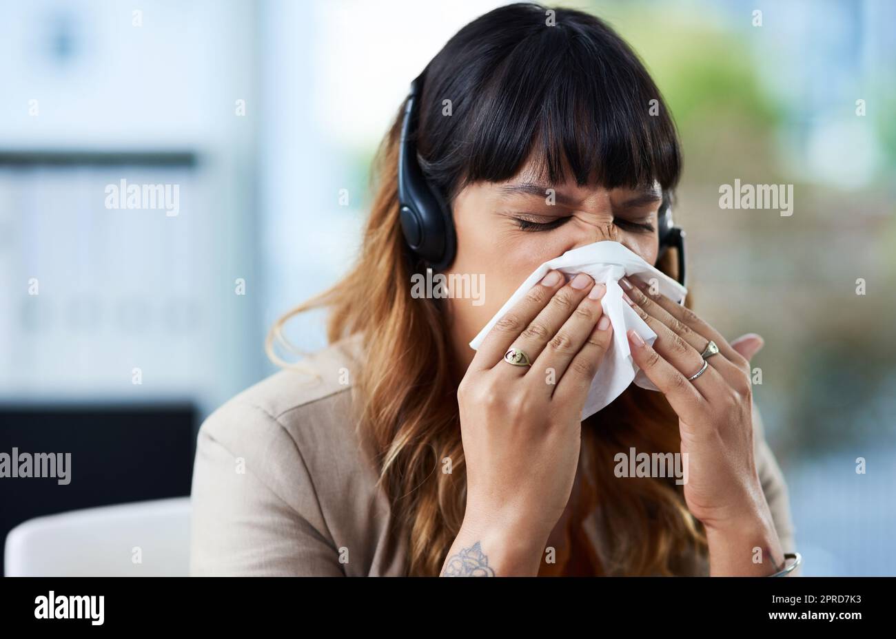 Will questo freddo solo Vai via. una giovane donna d'affari attraente che soffre di un freddo e soffiare il naso mentre nel suo ufficio. Foto Stock