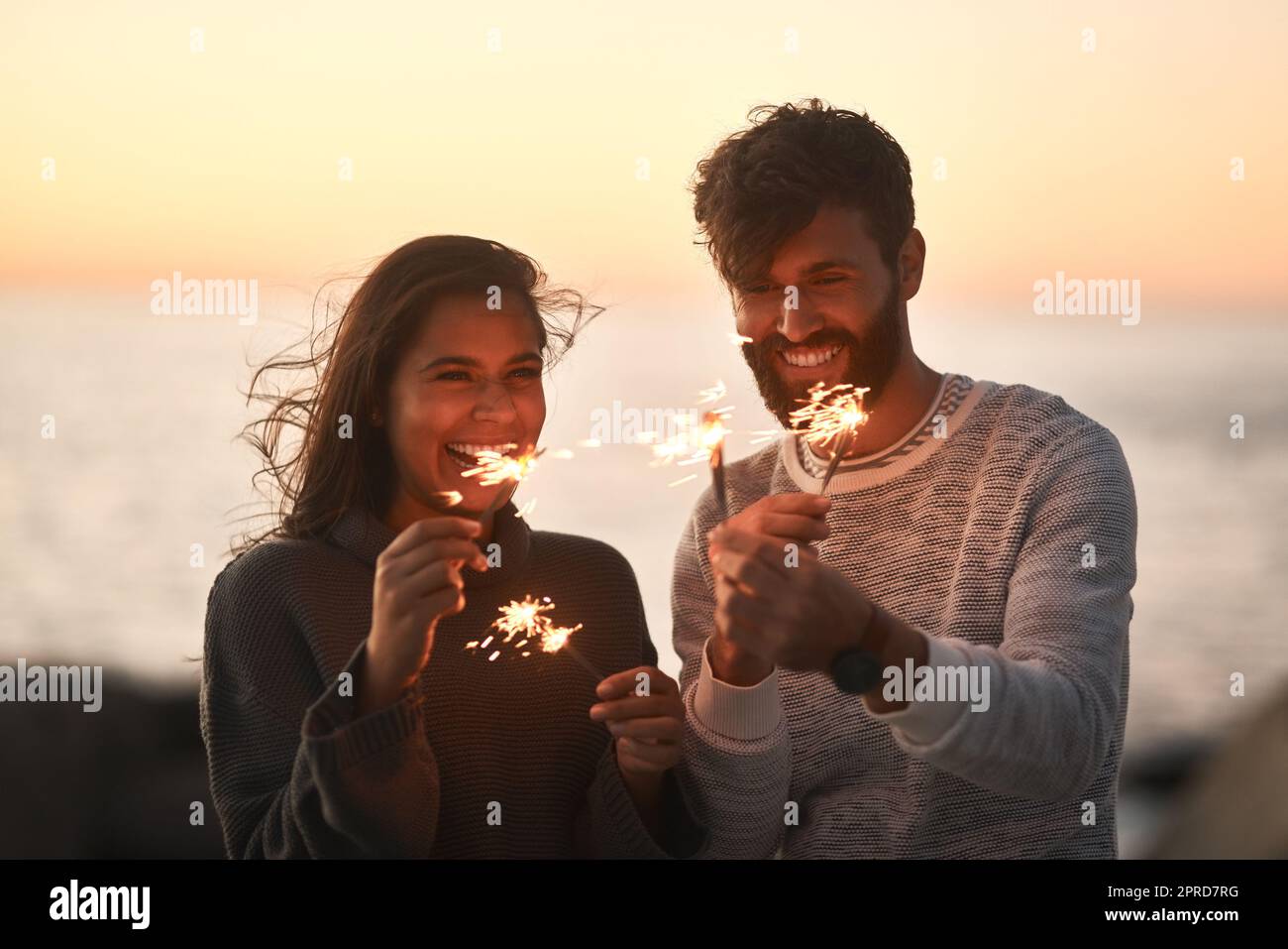 L'amore è la fiamma ardente della vita. Una giovane coppia felice che si diverte con gli scintillanti sulla spiaggia al tramonto. Foto Stock
