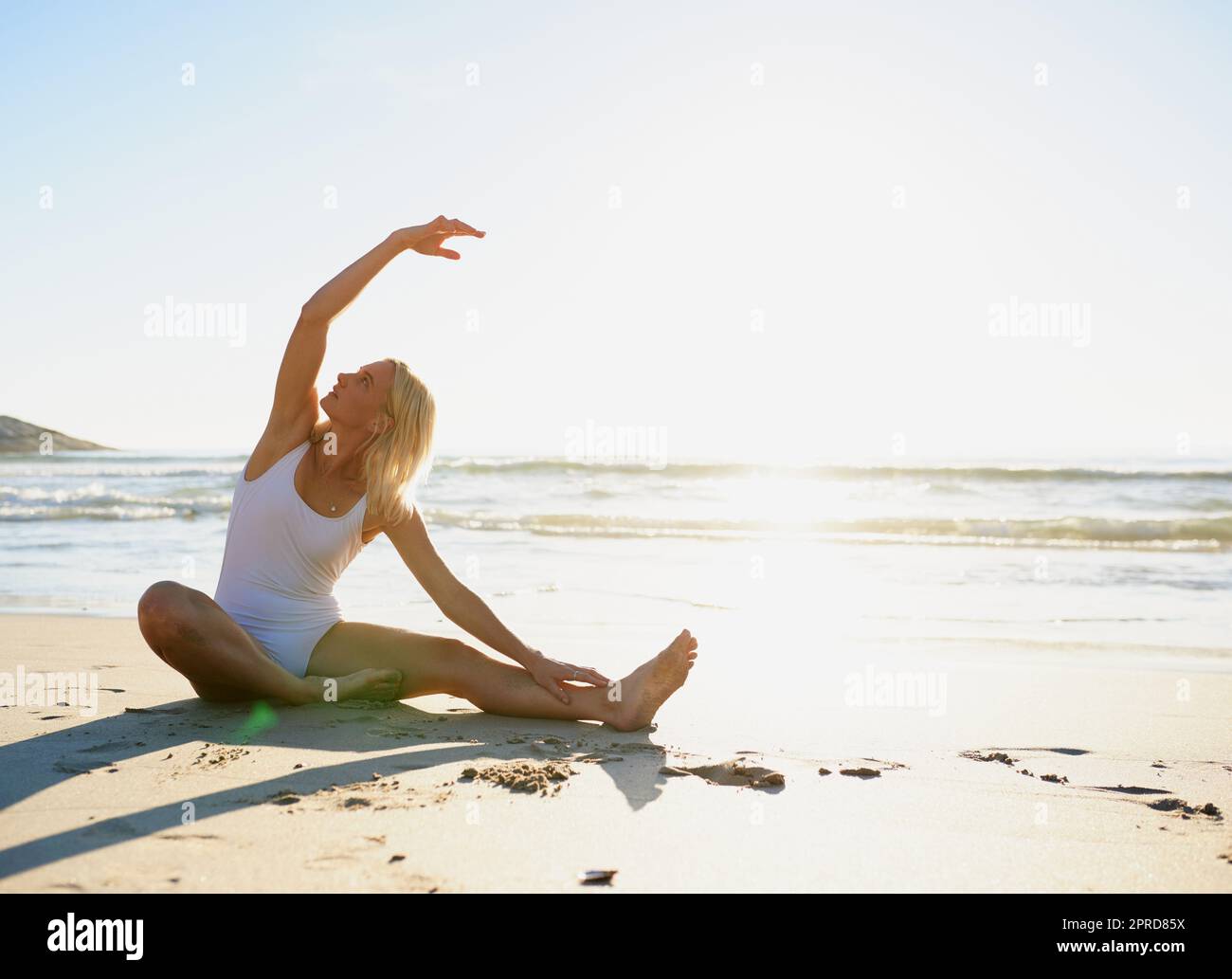 Respirare attraverso i tratti. Scatto a tutta lunghezza di una giovane donna attraente che fa una distesa di yoga presto la mattina sulla spiaggia. Foto Stock