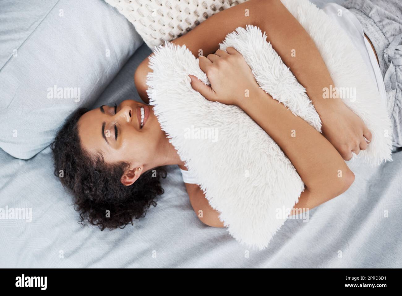 Innamorata del comfort, una giovane donna attraente che abbraccia un cuscino mentre si trova sul letto di casa. Foto Stock